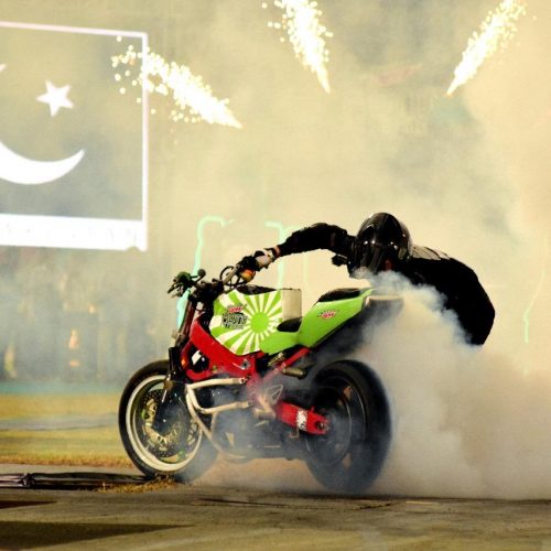stuntman riding superbike on ramp with Pakistani flag and fireworks
